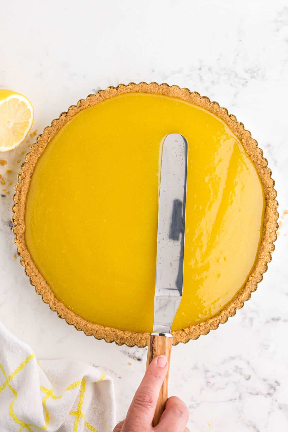 spreading lemon curd mixture into the shortbread crust and tart pan with a metal offset knife