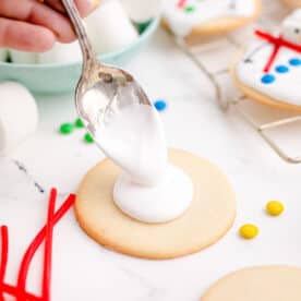 a metal spoon drops a dollop of icing on top of a sugar cookie