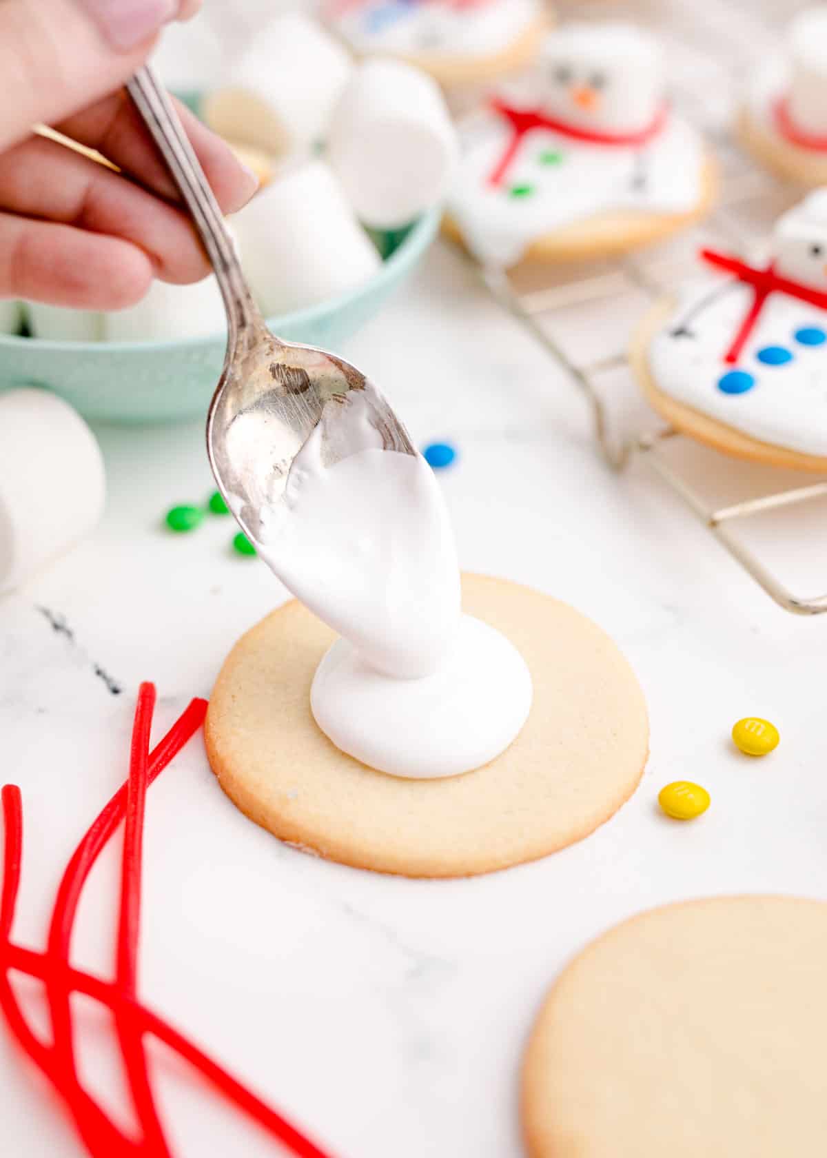 a metal spoon drops a dollop of icing on top of a sugar cookie