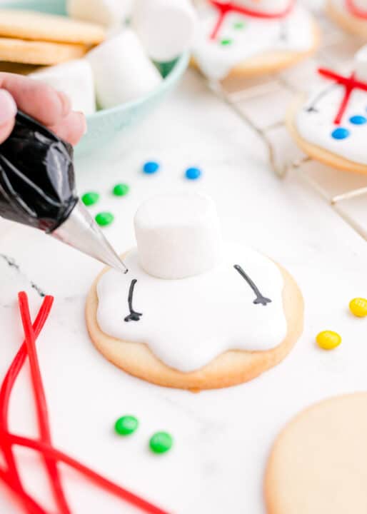 black arms are being piped onto the icing for the snowman