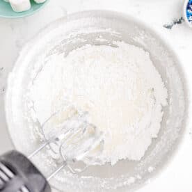 an electric hand mixer beating together powdered sugar and water in a bowl