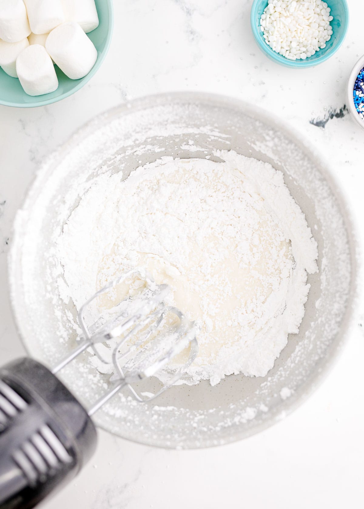 an electric hand mixer beating together powdered sugar and water in a bowl