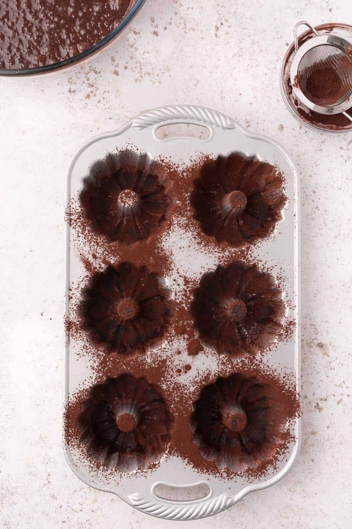 metal mini bundt pans are dusted with cocoa powder