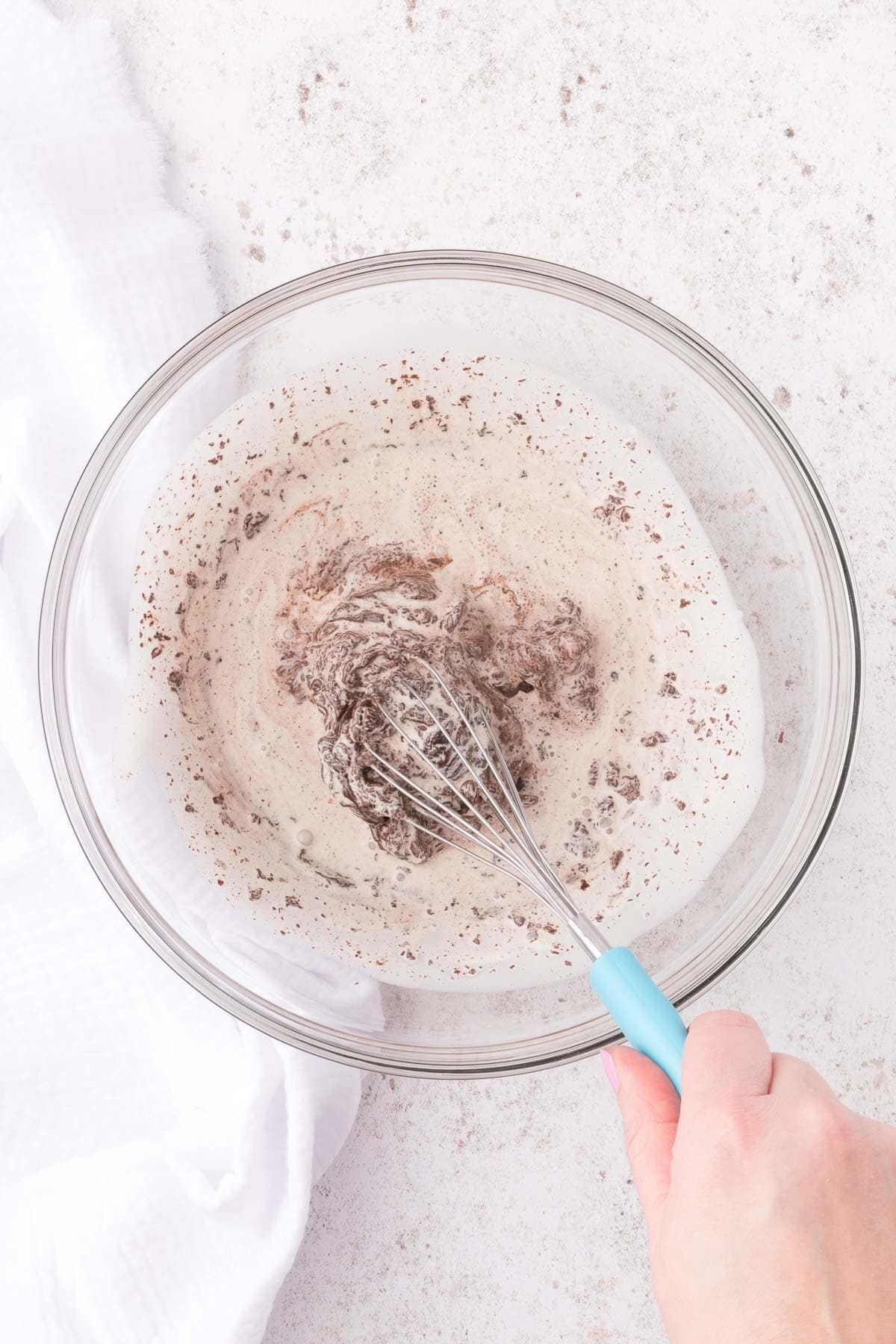 whisking together cream and chopped chocolate in a glass bowl