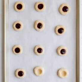 indentions made into raspberry thumbprint cookie dough and raspberry jam being filled in the cavity