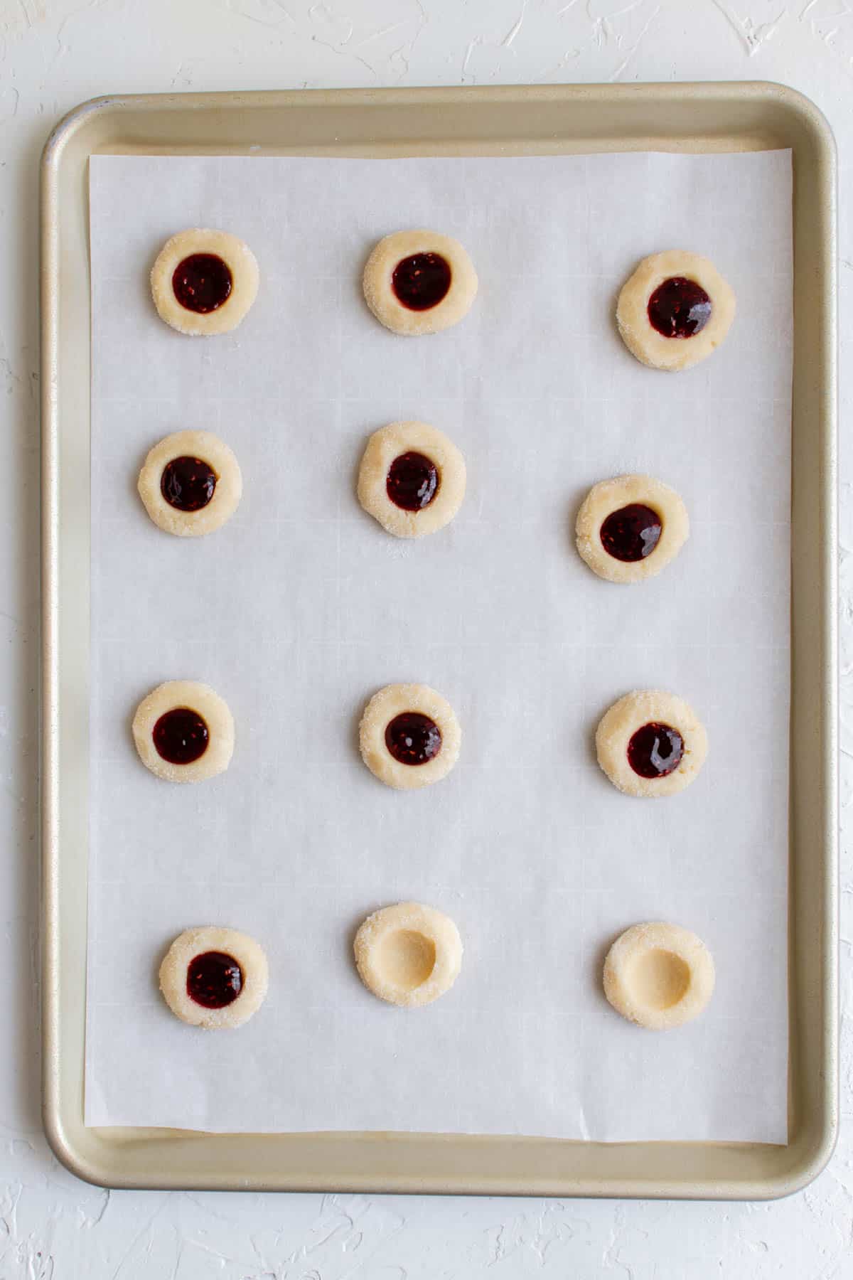 indentions made into raspberry thumbprint cookie dough and raspberry jam being filled in the cavity