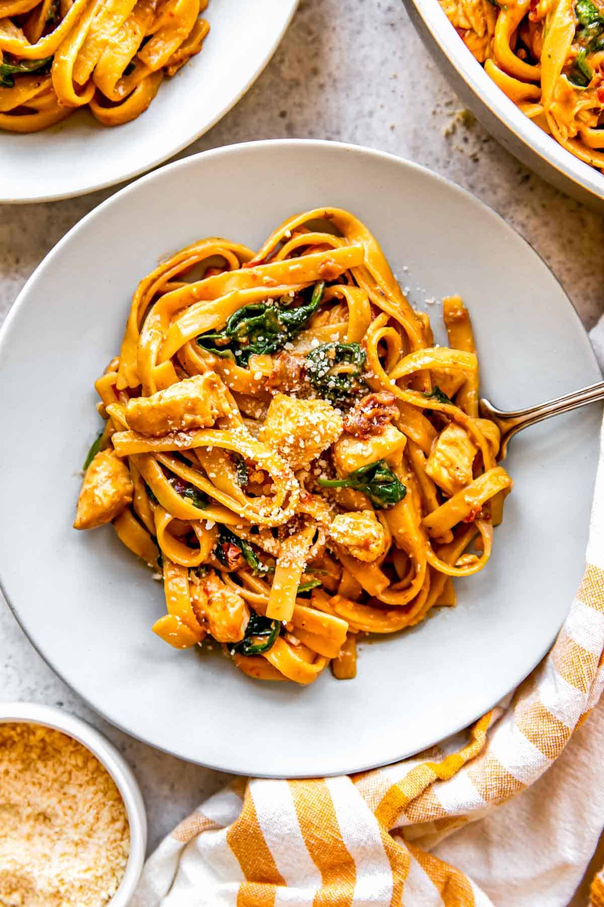 a bowl of sun-dried tomato chicken pasta with grated parmesan cheese on top