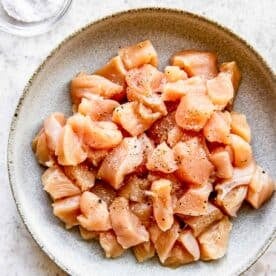 raw chicken in a bowl sprinkled with salt and ground black pepper