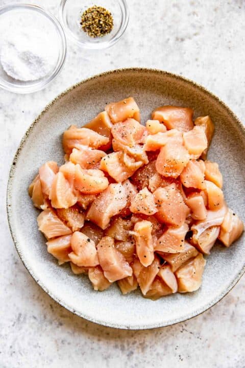 raw chicken in a bowl sprinkled with salt and ground black pepper