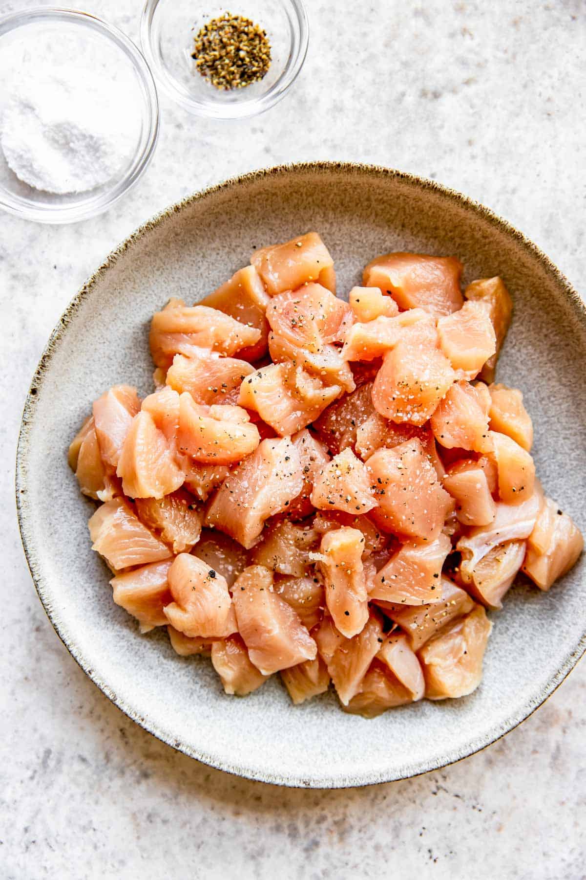 raw chicken in a bowl sprinkled with salt and ground black pepper