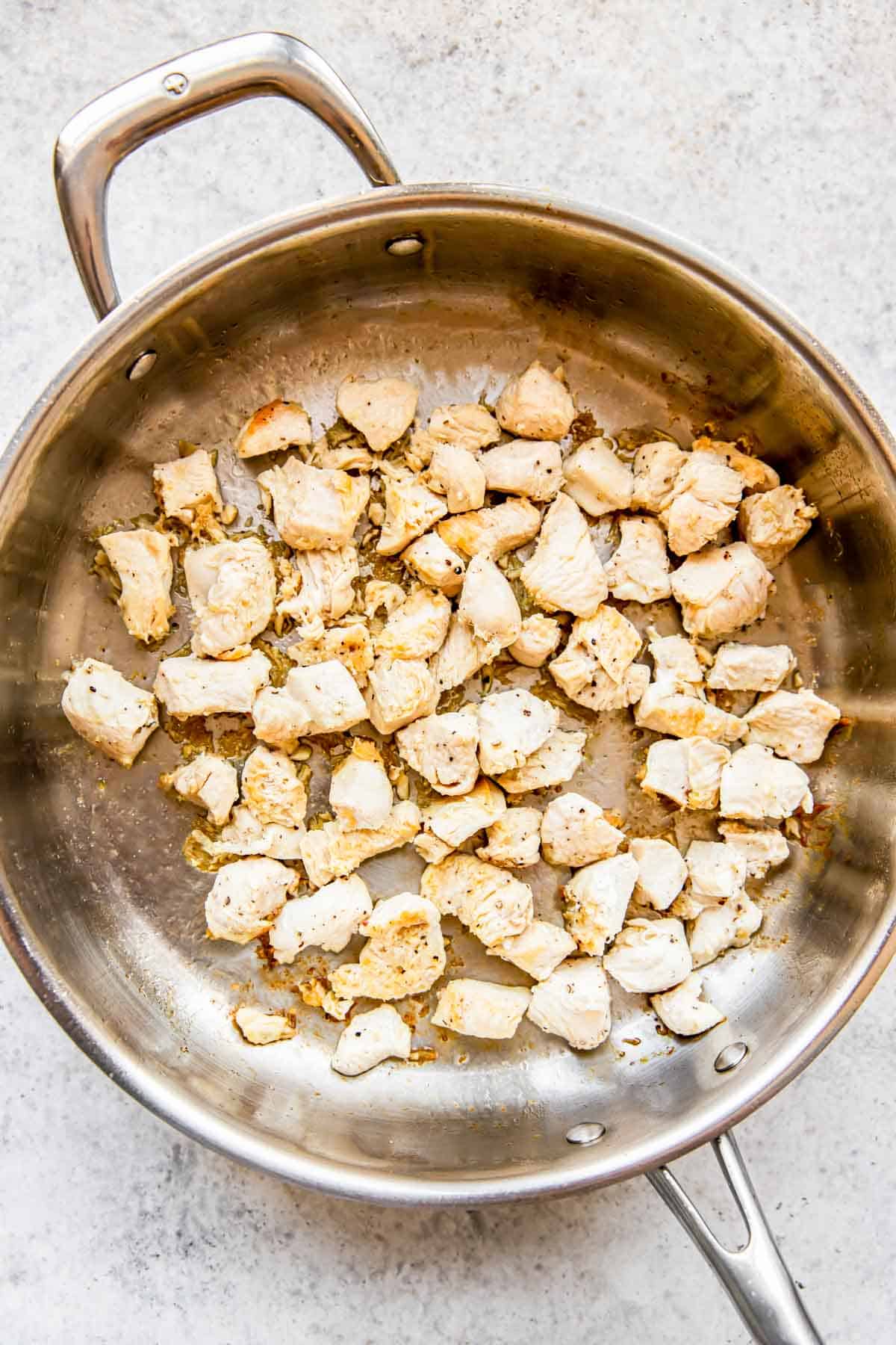 chicken in a stainless steel pan being cooked and browned