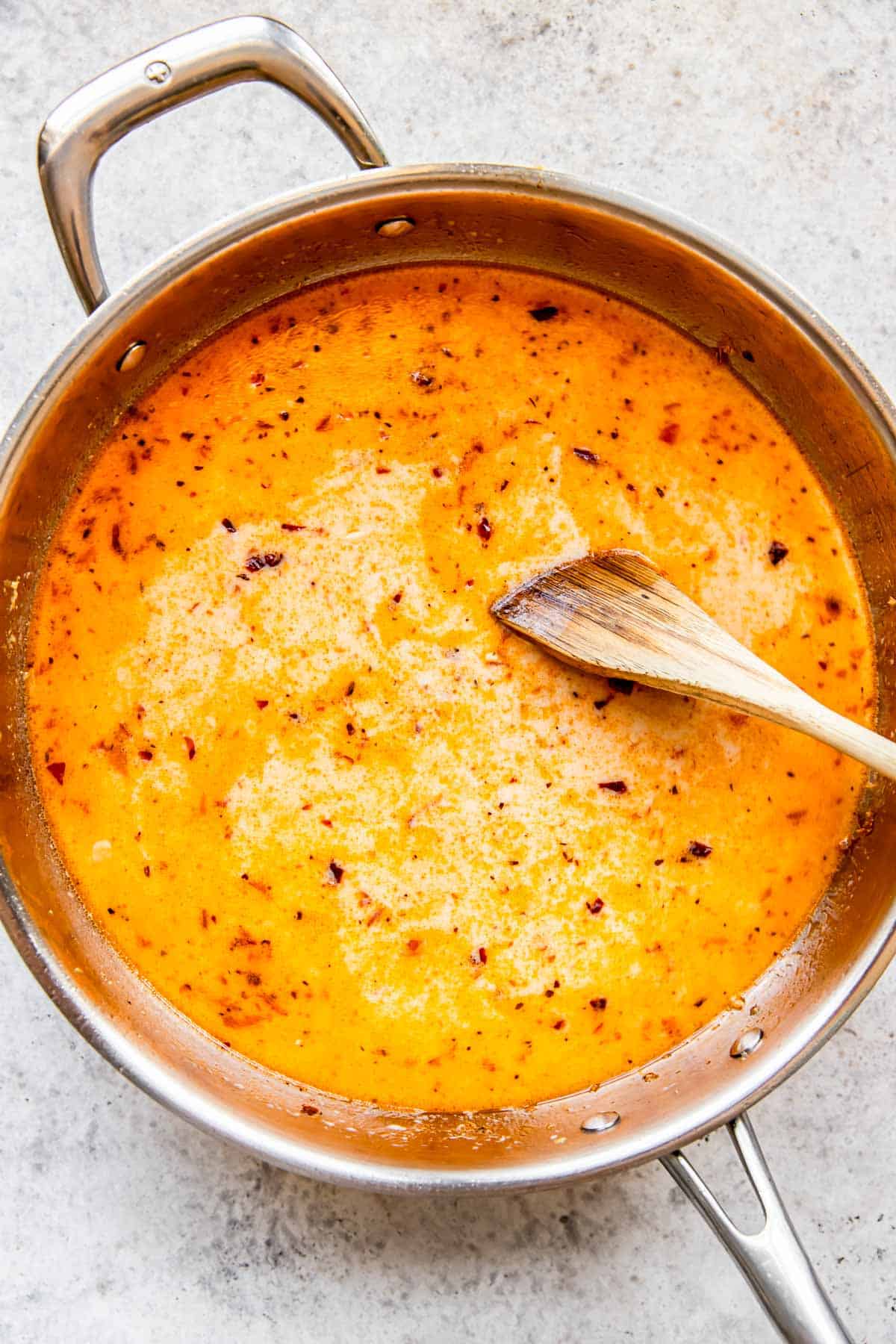 creamy liquid in stainless steel pan being stirred with a wooden spoon