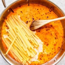 dry linguine pasta added to a stainless steel skillet with liquid and wooden spoon