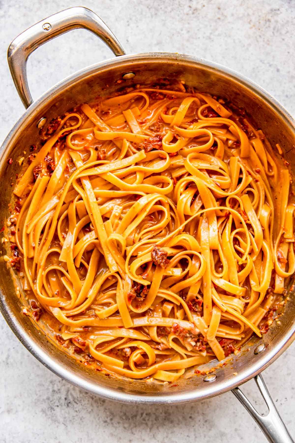 linguine pasta cooked through and in a cream sauce in a stainless steel skillet