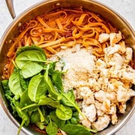 fresh spinach, parmesan cheese, and cooked chicken added to the pasta in the stainless steel skillet