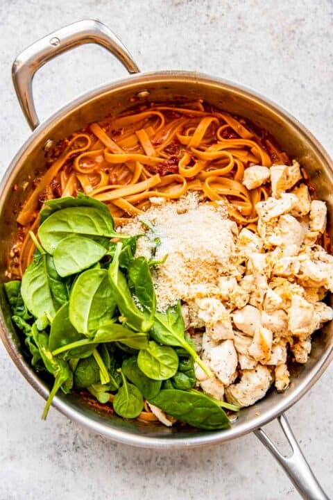 fresh spinach, parmesan cheese, and cooked chicken added to the pasta in the stainless steel skillet