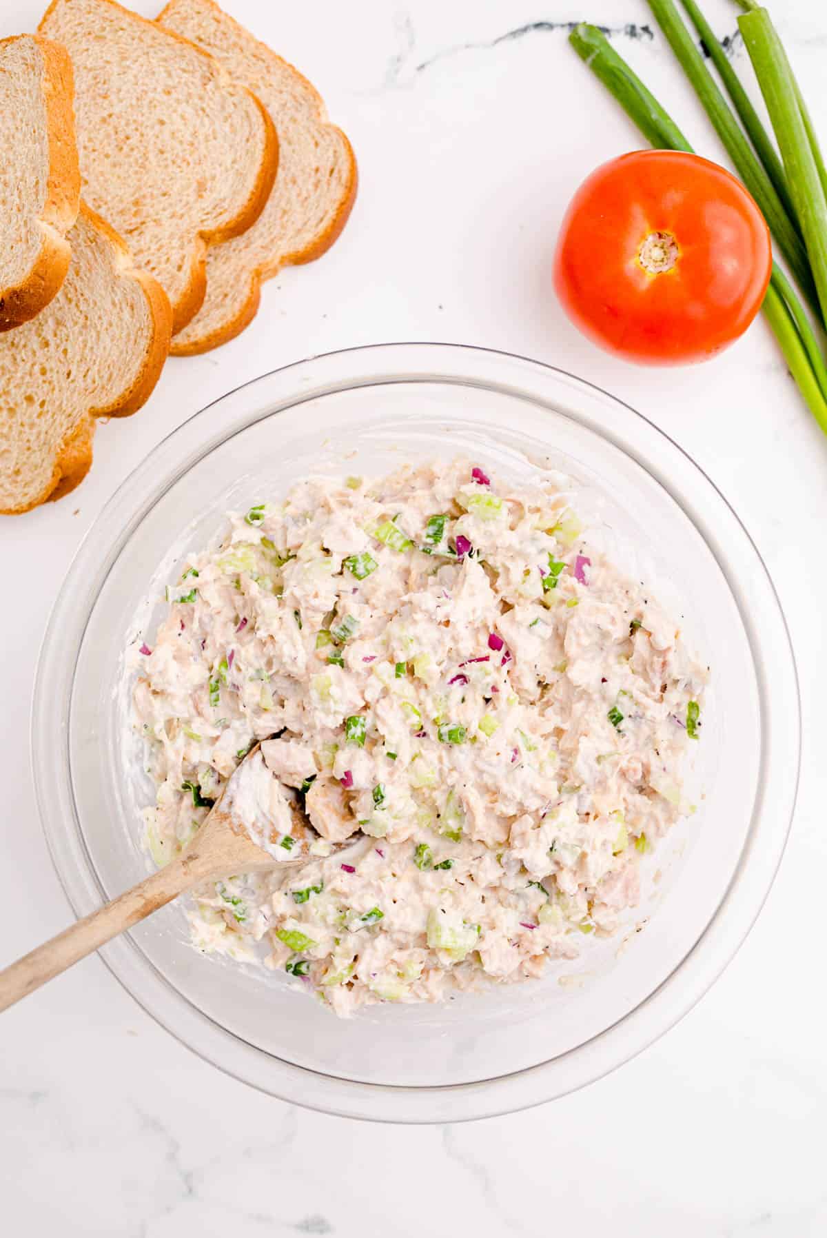 ingredients for tuna melt all mixed together in a clear bowl with a wooden spoon