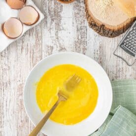 a shallow plate with eggs have been beaten with a metal gold fork