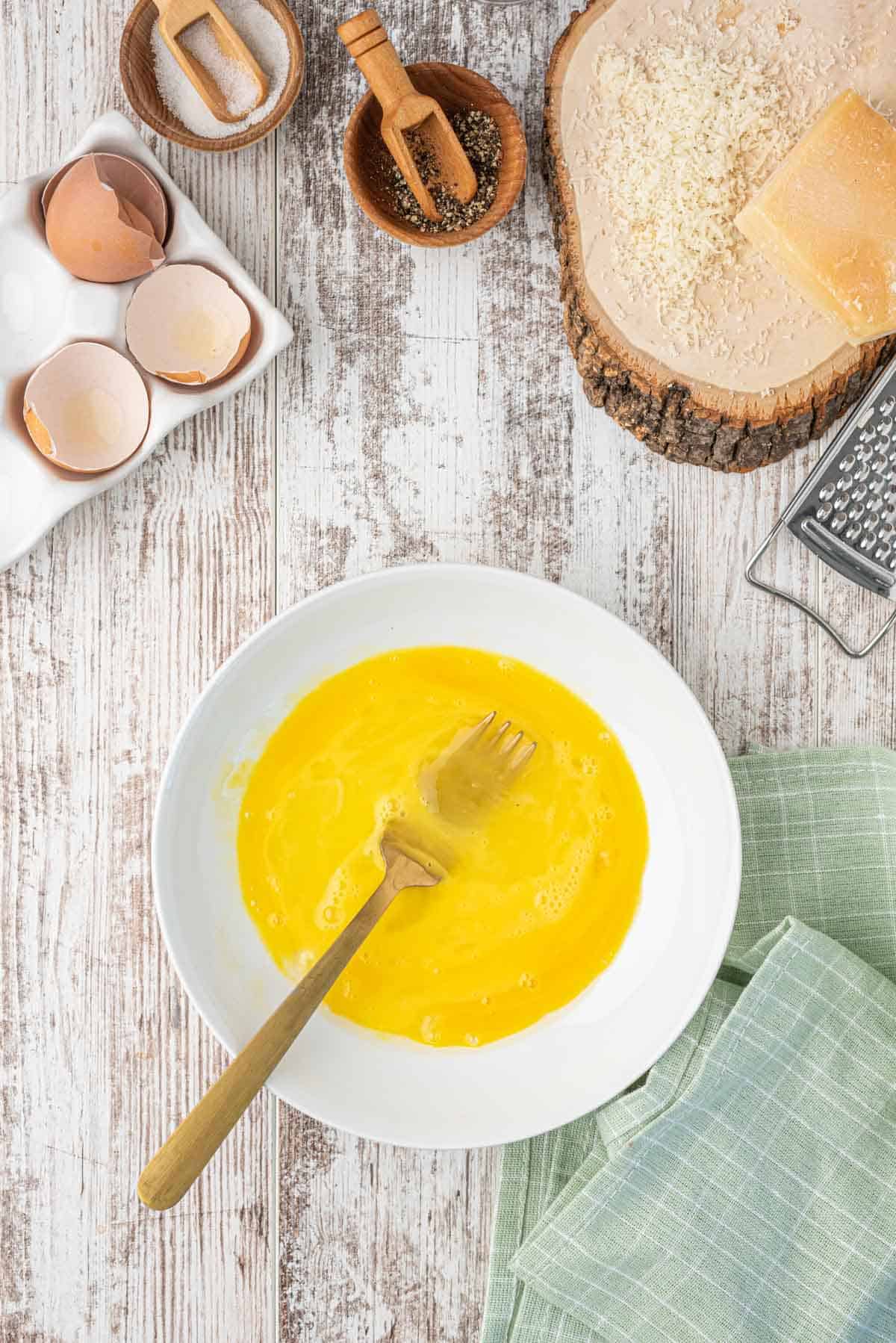 a shallow plate with eggs have been beaten with a metal gold fork