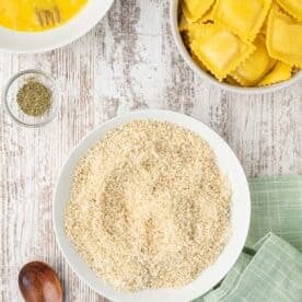 panko breadcrumbs and parmesan cheese on a shallow white plate next to a wooden spoon