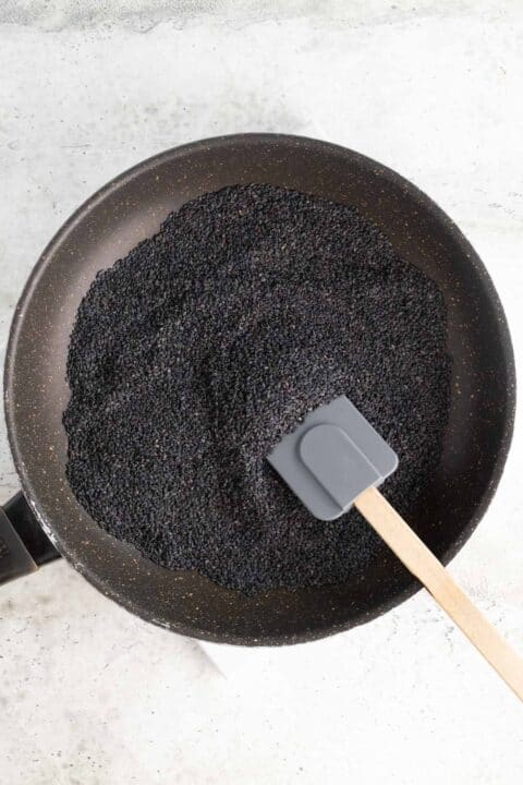 a large amount of black sesame seeds in a skillet with a silicone spatula