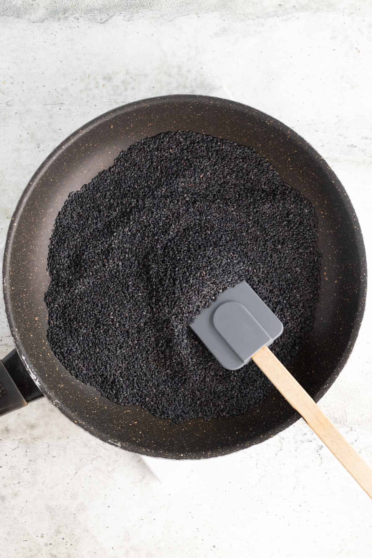 a large amount of black sesame seeds in a skillet with a silicone spatula