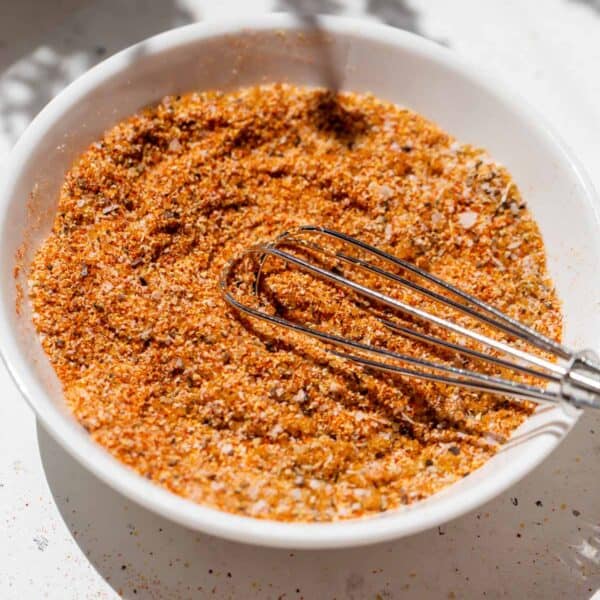 a metal whisk in burger seasoning on a small white dish