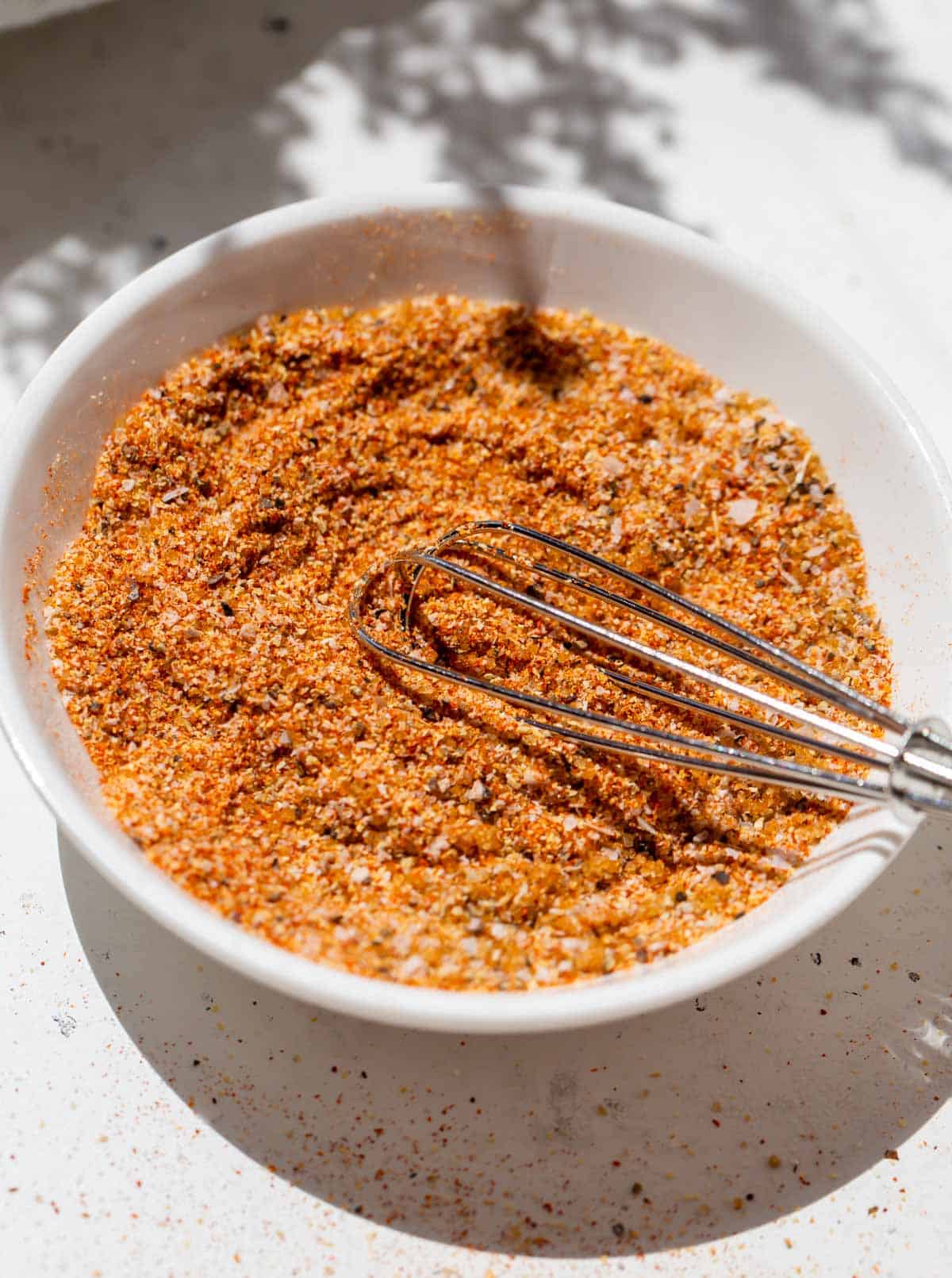 a metal whisk in burger seasoning on a small white dish