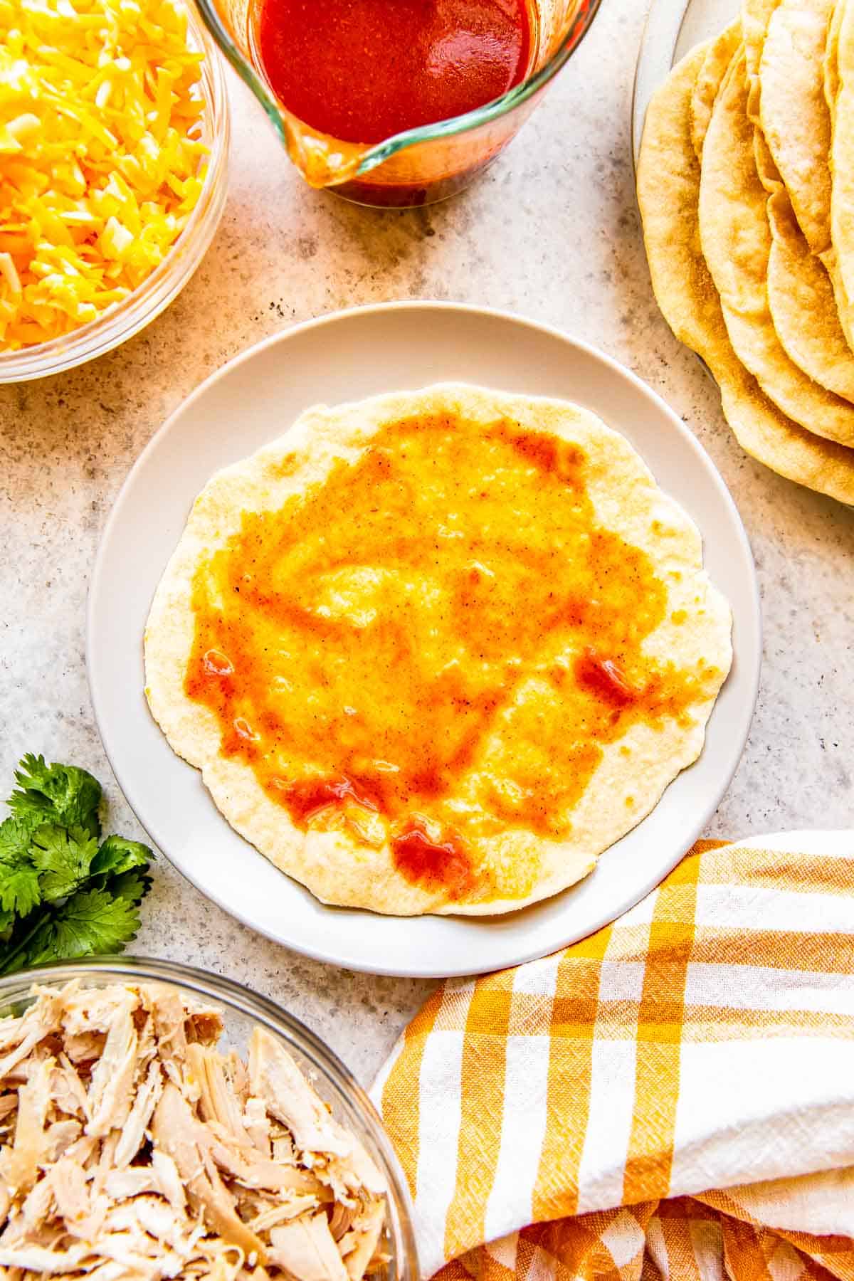 red enchilada sauce spread onto a flour tortilla on a plate