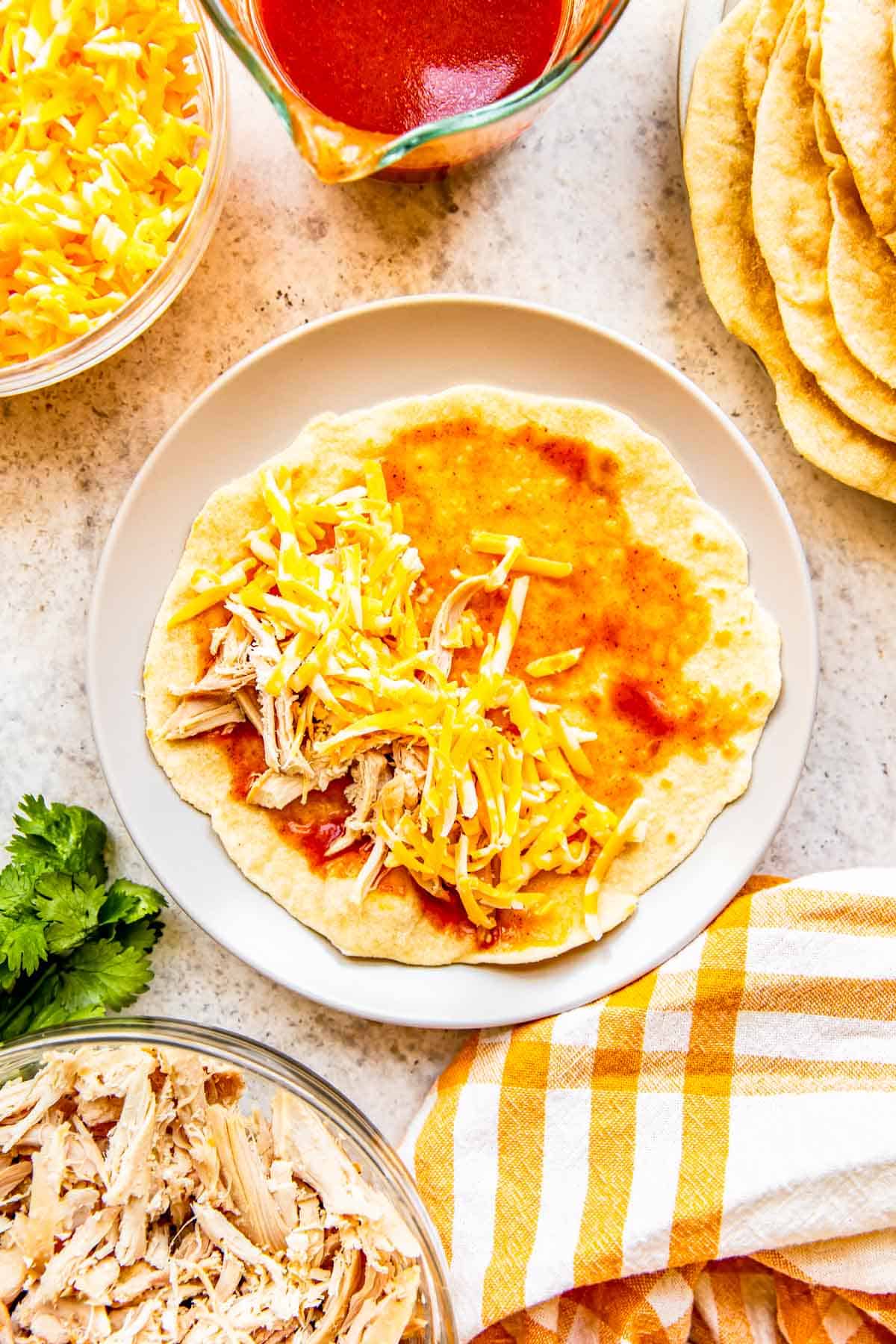 shredded chicken and shredded cheese added on top of flour tortilla with red enchilada sauce