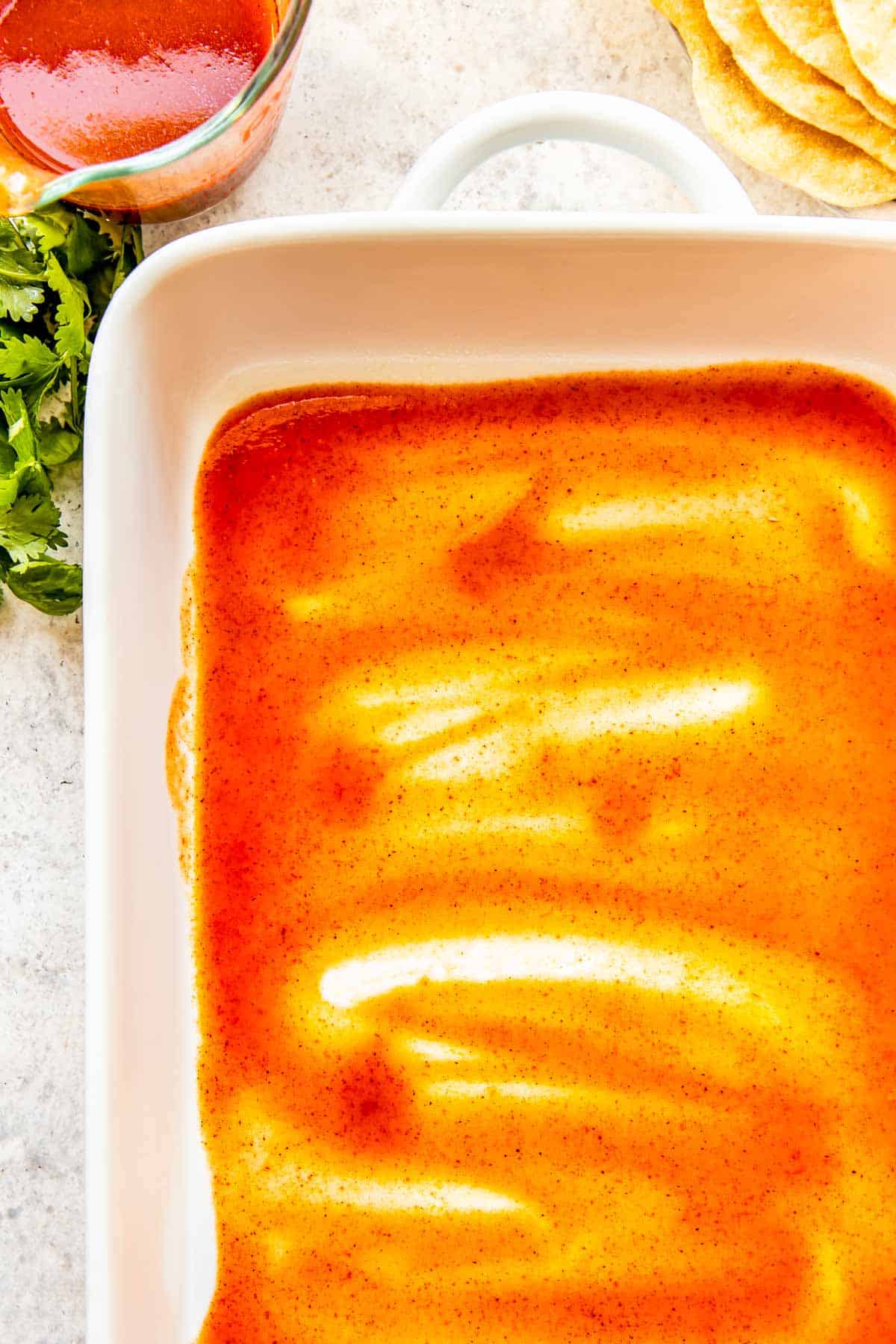 red enchilada sauce spread into the bottom of a white baking dish