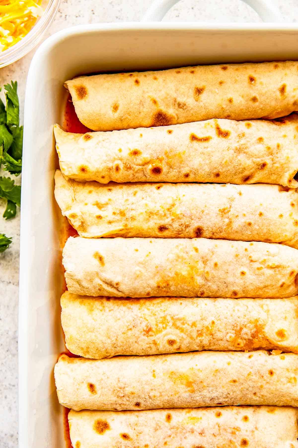 chicken enchiladas assembled and placed into a white baking dish