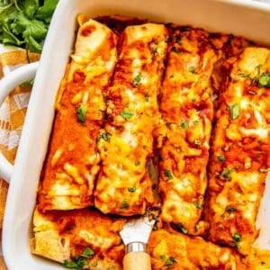 a metal spatula underneath a chicken enchilada in a white baking dish