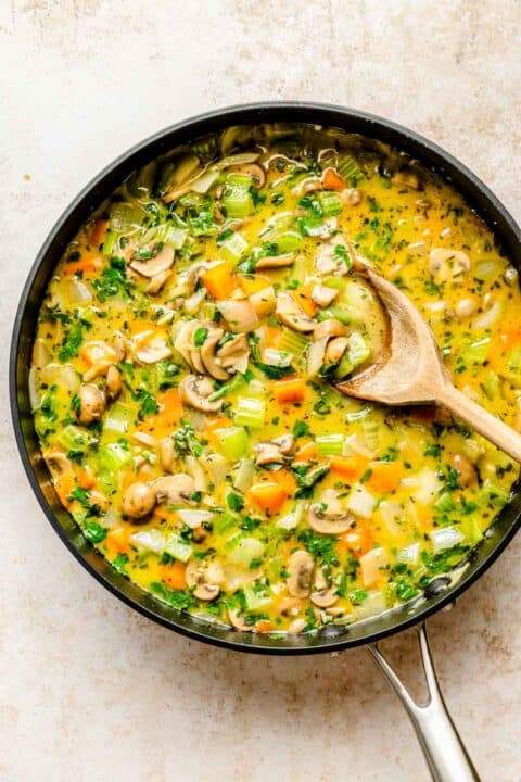 vegetables and chicken broth in a skillet with a wooden spoon