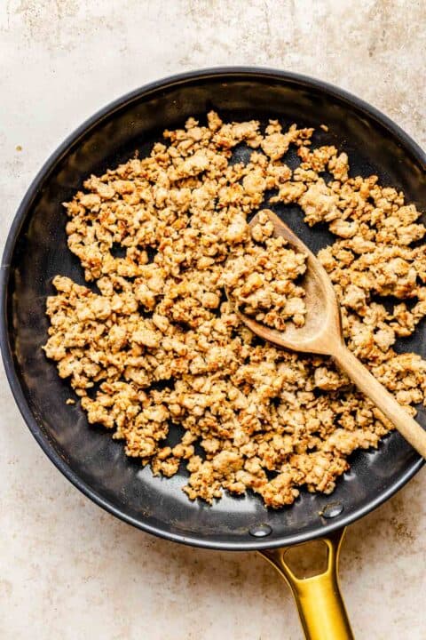 crumbled sausage in a skillet with a wooden spoon