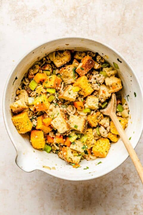 cornbread, sourdough, and vegetable mixture in a large mixing bowl with a wooden spoon