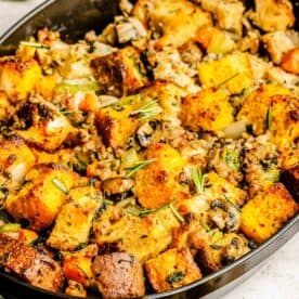 cornbread stuffing in a large black cast iron baking dish with fresh rosemary sprinkled on top