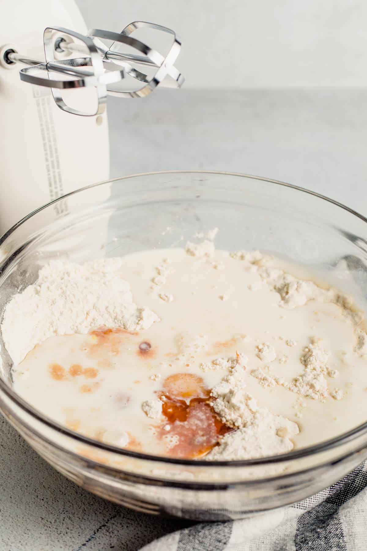 flour and wet ingredients in a large clear bowl next to an electric hand mixer