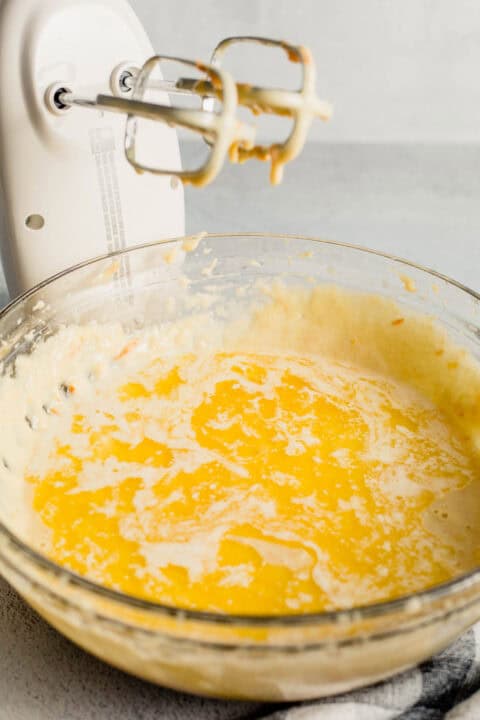melted butter added to a large bowl with flour next to an electric hand mixer