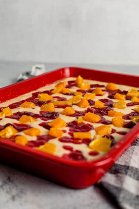 fresh orange chunks put on top of the cranberry sauce in the red baking dish