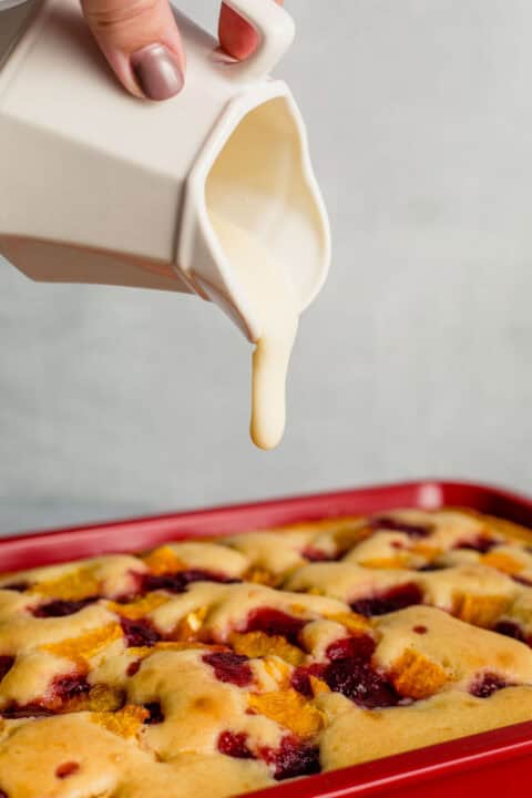 glaze is being poured out of a white ceramic container on top of the baked breakfast cake