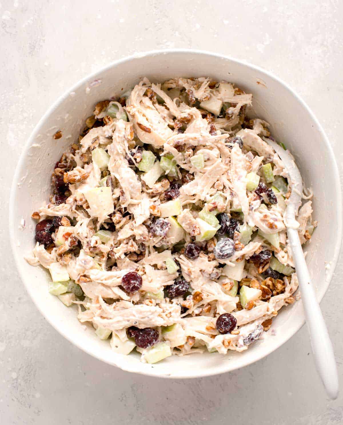 all the ingredients for the cranberry pecan chicken salad is mixed together in a large white bowl with a silicone spoon