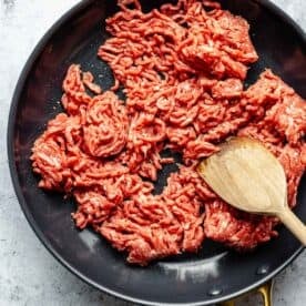 ground beef in a nonstick skillet being broken into smaller pieces with a wooden spatula