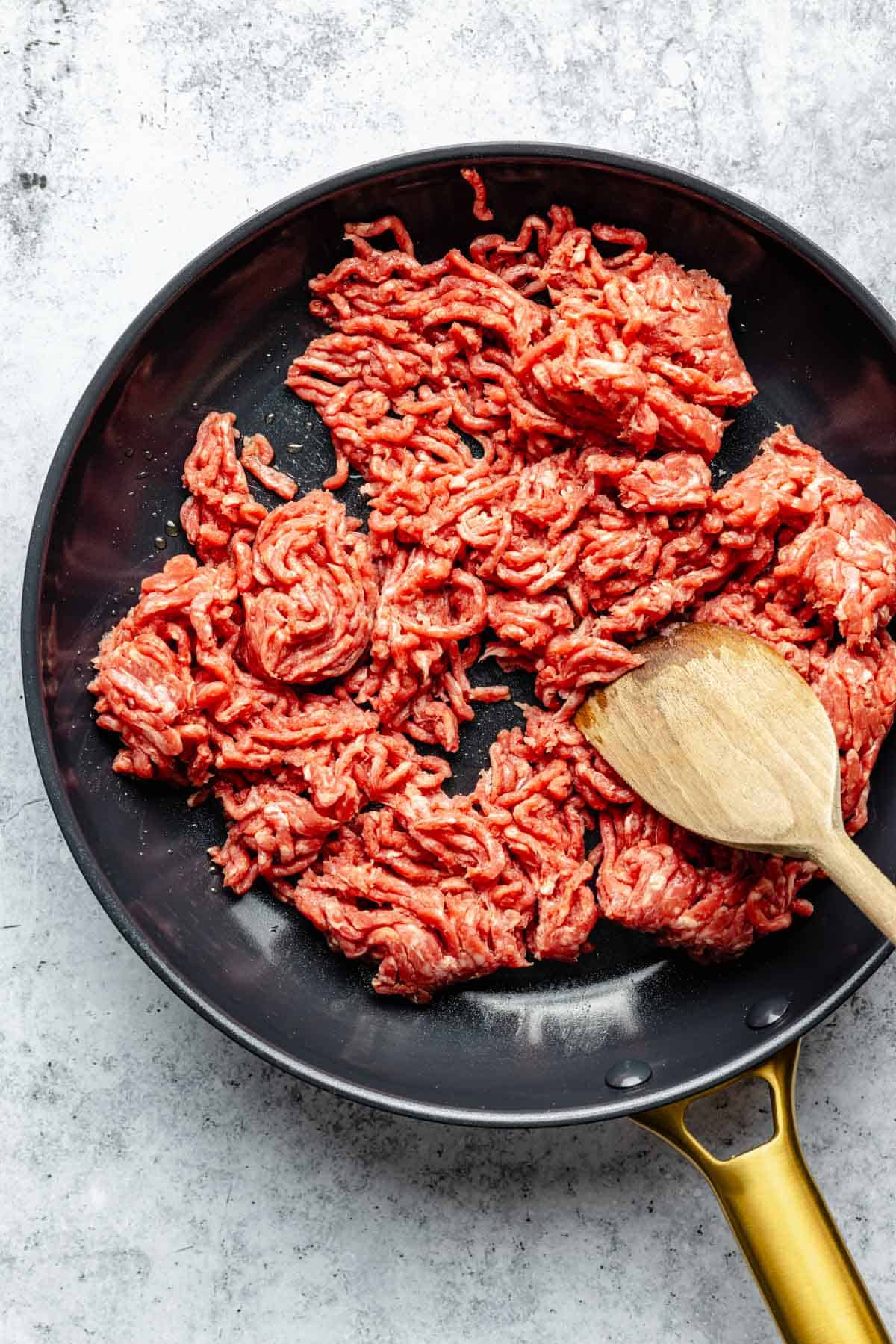 ground beef in a nonstick skillet being broken into smaller pieces with a wooden spatula