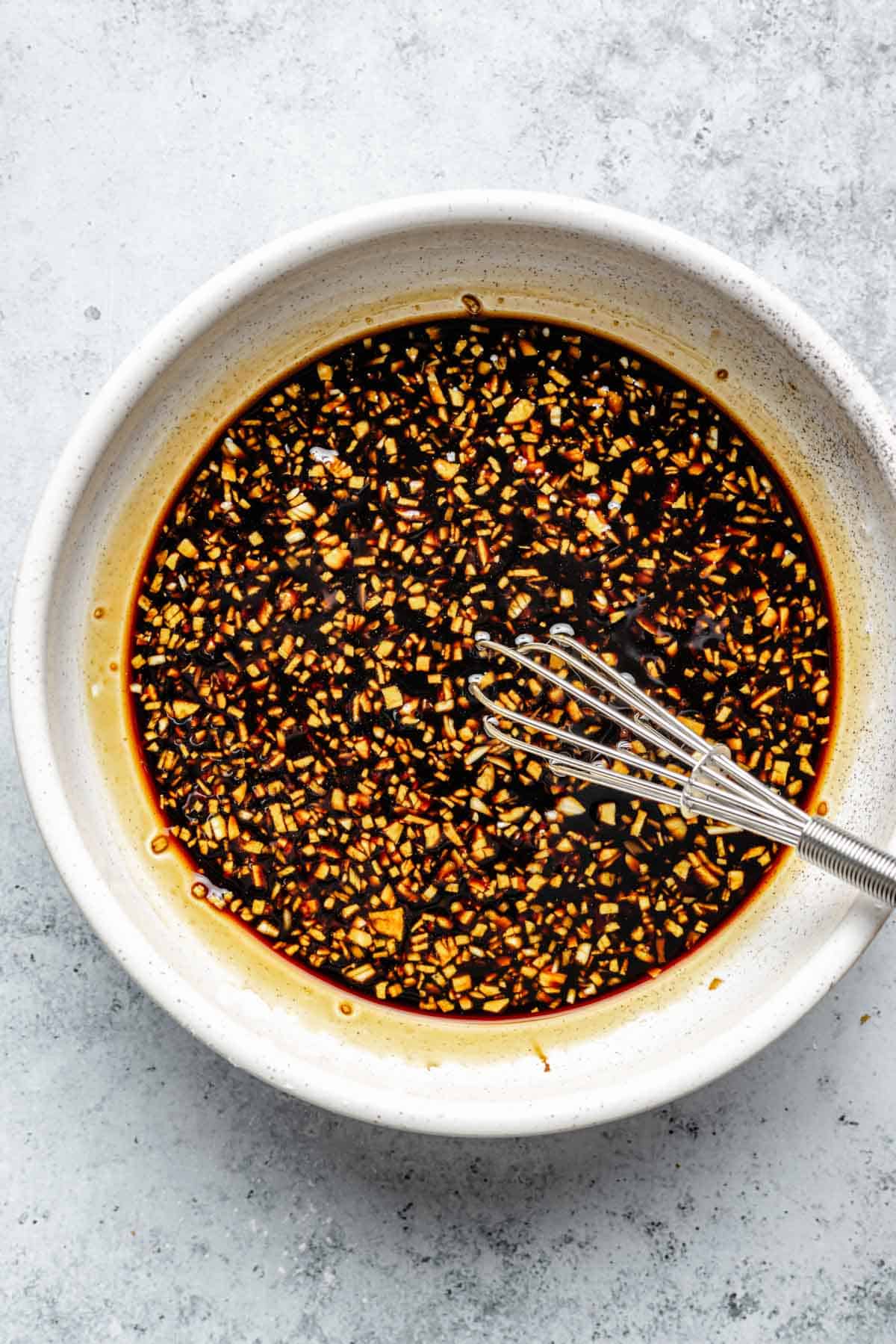 soy sauce-based sauce with minced garlic and ginger in a bowl with a metal whisk