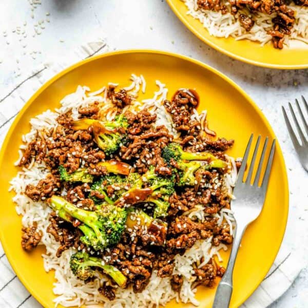 ground beef and broccoli plated on bright yellow plates on a bed of jasmine rice with a metal fork on the plate