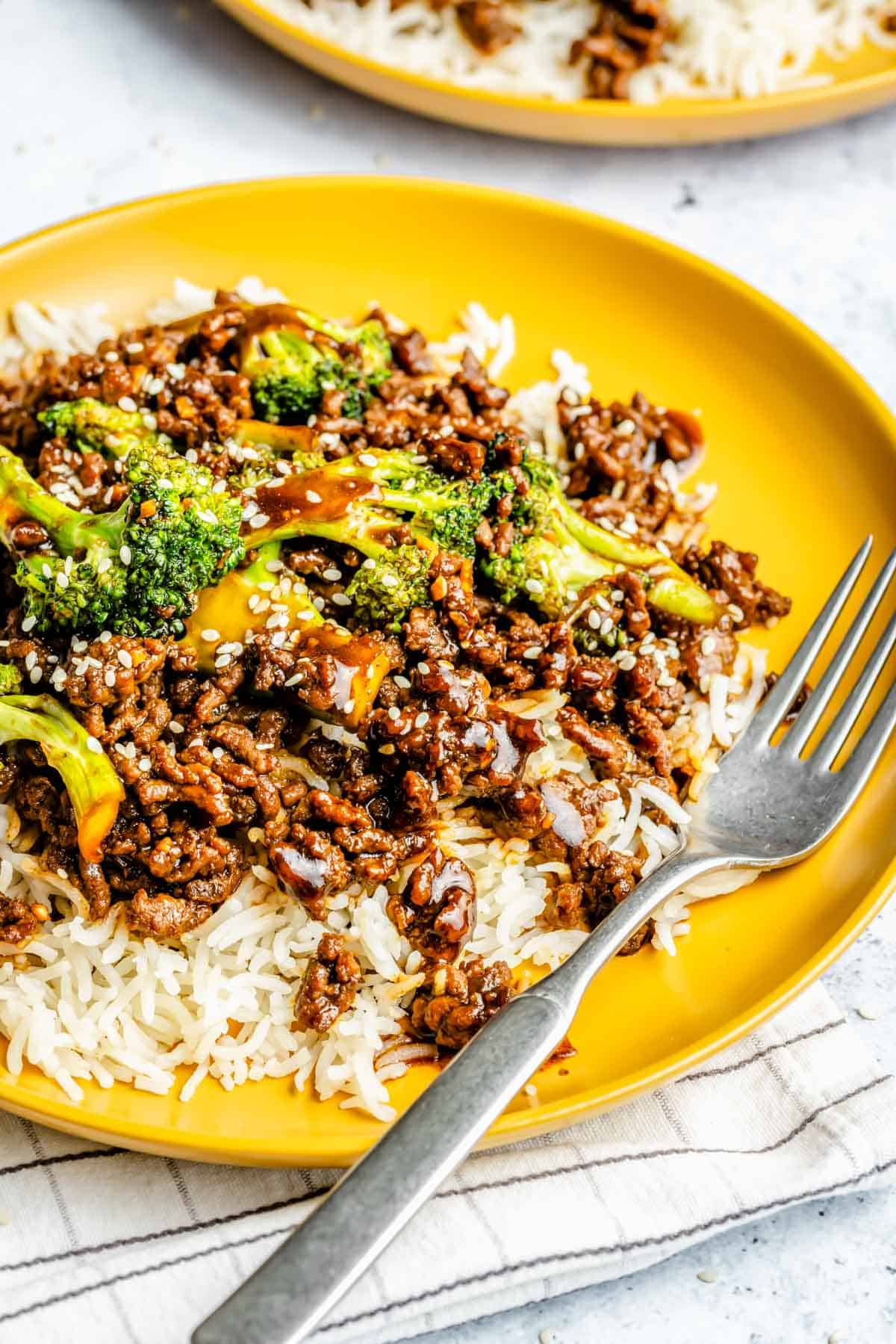 a metal fork lays on top of a bright yellow plate with ground beef and broccoli and jasmine rice
