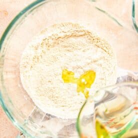 flour in a glass standing mixer bowl with oil being added to the bowl