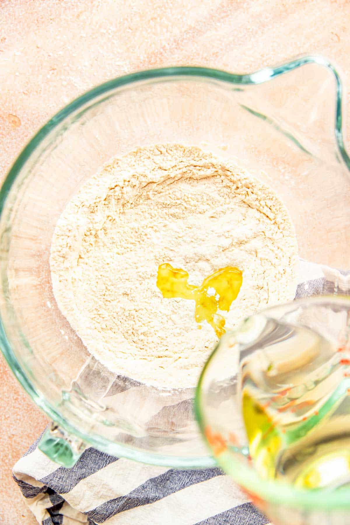flour in a glass standing mixer bowl with oil being added to the bowl