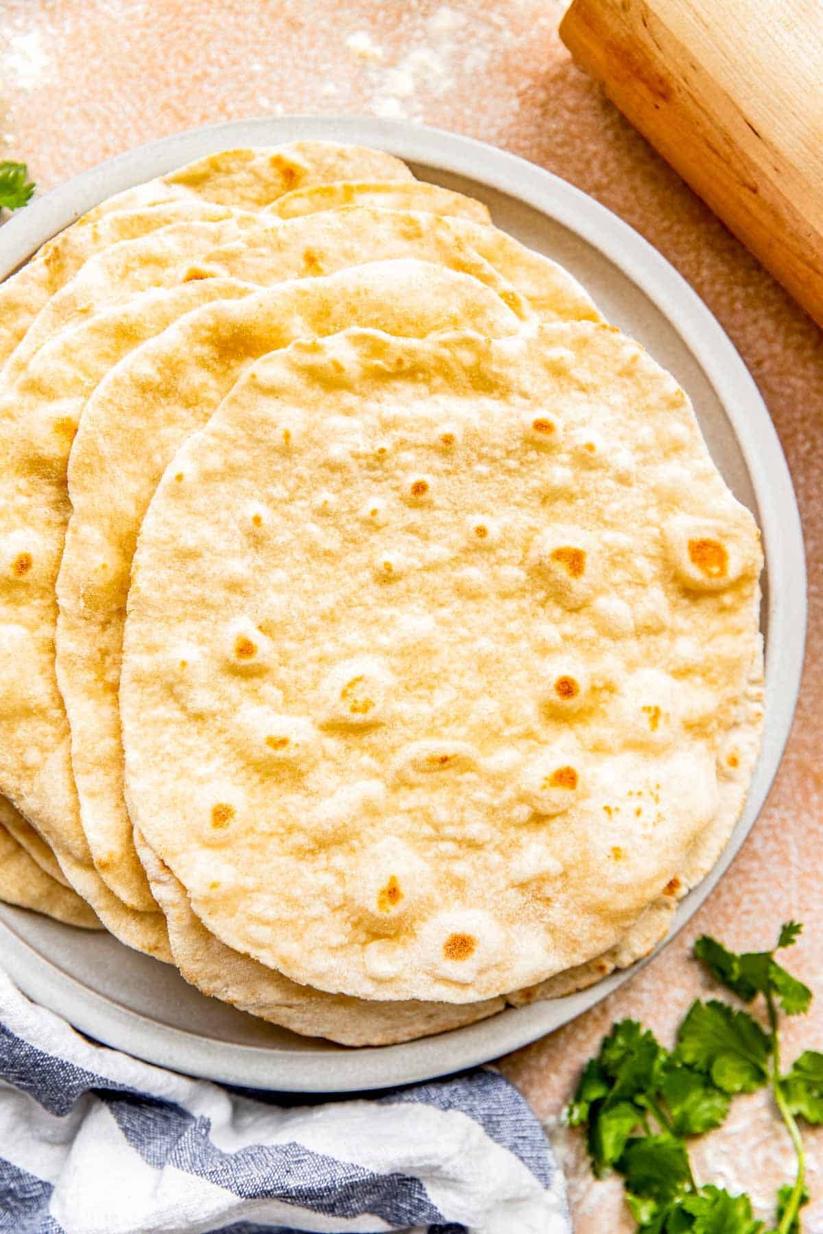 flour tortillas stacked on a plate next to a striped linen towel